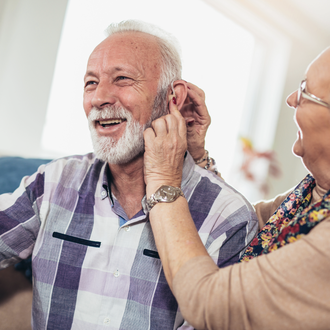 An elderly man smiling as his hearing aid is fitted