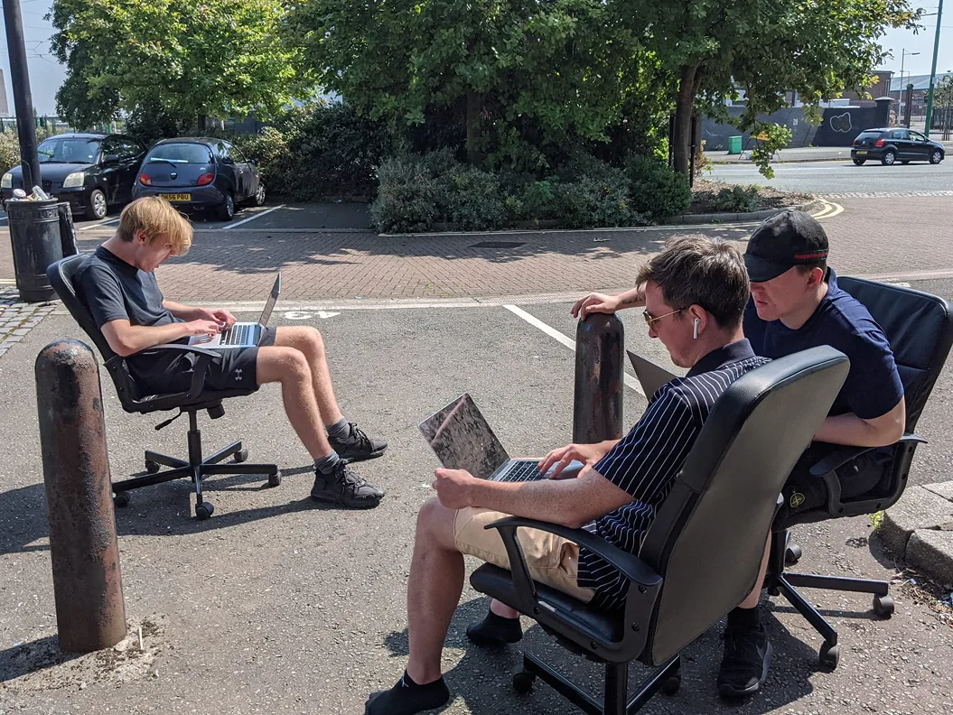 Three of the team working on laptops from office chairs outside during lockdown